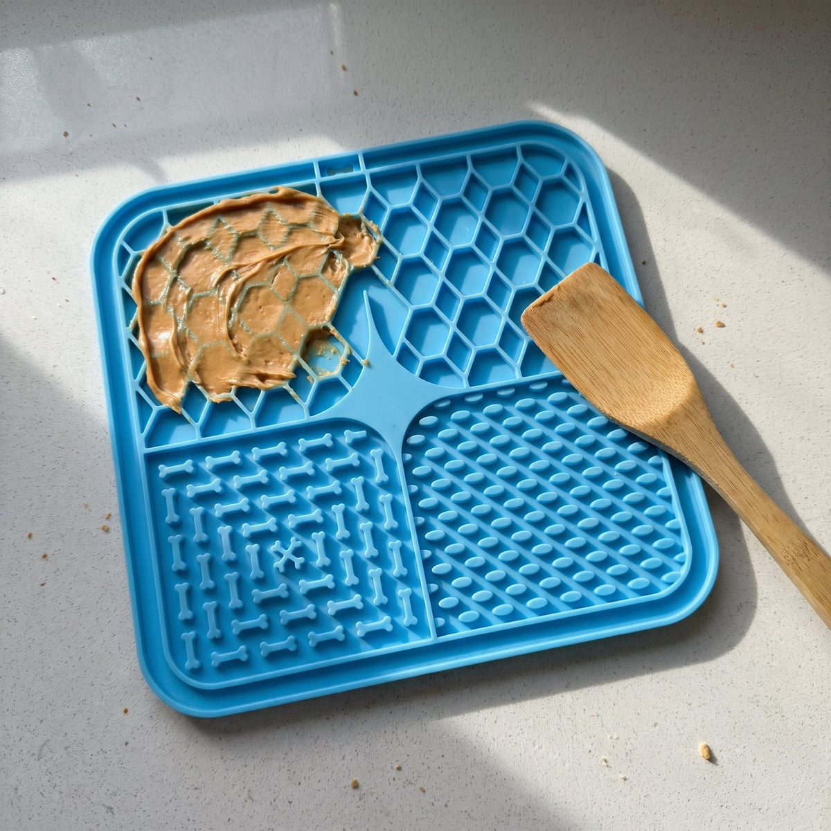 Blue lick mat on a kitchen counter with peanut butter and a wooden spatula